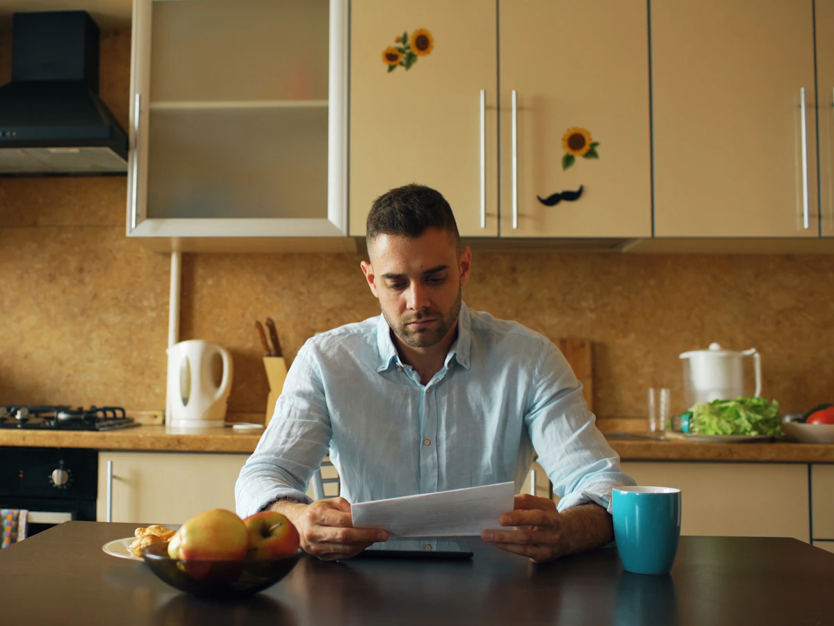 A man reviewing a bill at his kitchen table with a cup of coffee
