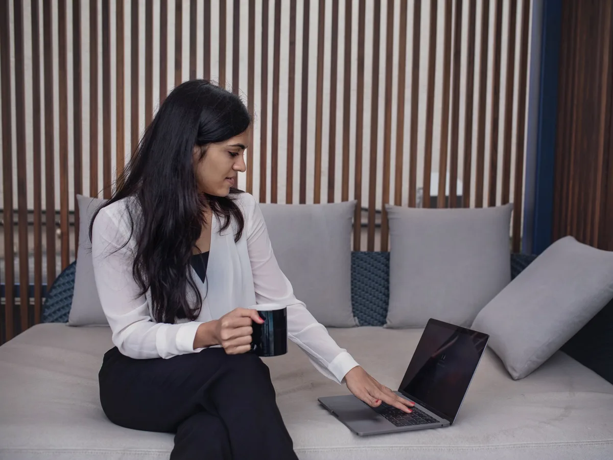 A woman on a sofa with a mug of coffee, calmly checking her laptop