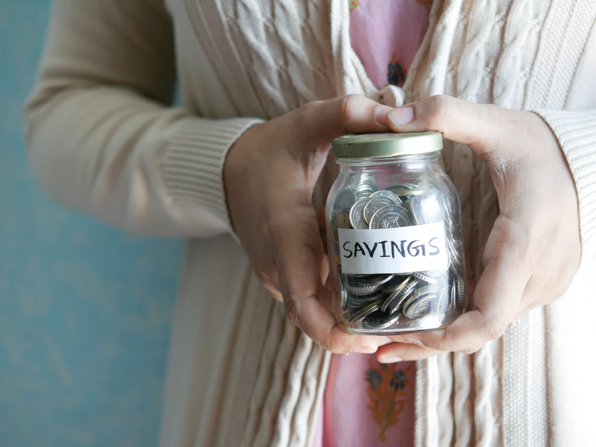 Hands holding a sealed glass jar labeled Savings