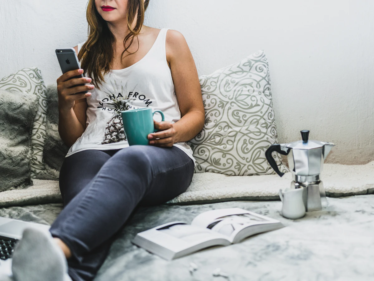 A person relaxing at home, checking their phone with a cup of coffee