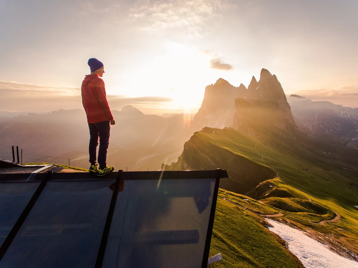 A hiker in a red jacket watching the sun rise over mountain peaks